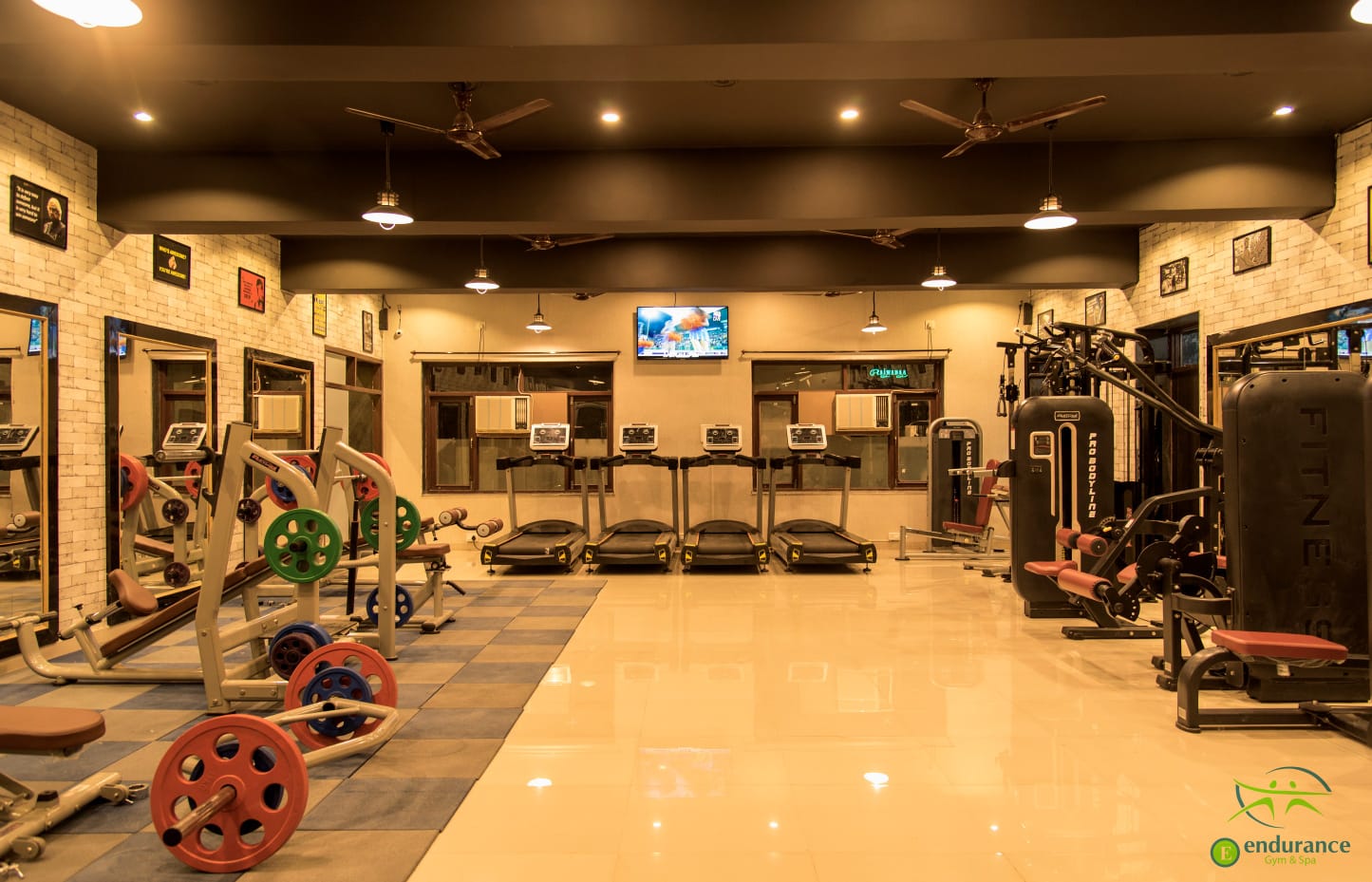 A wide picture of a gym focused on weight rack and in distance a girl doing dumbell rows